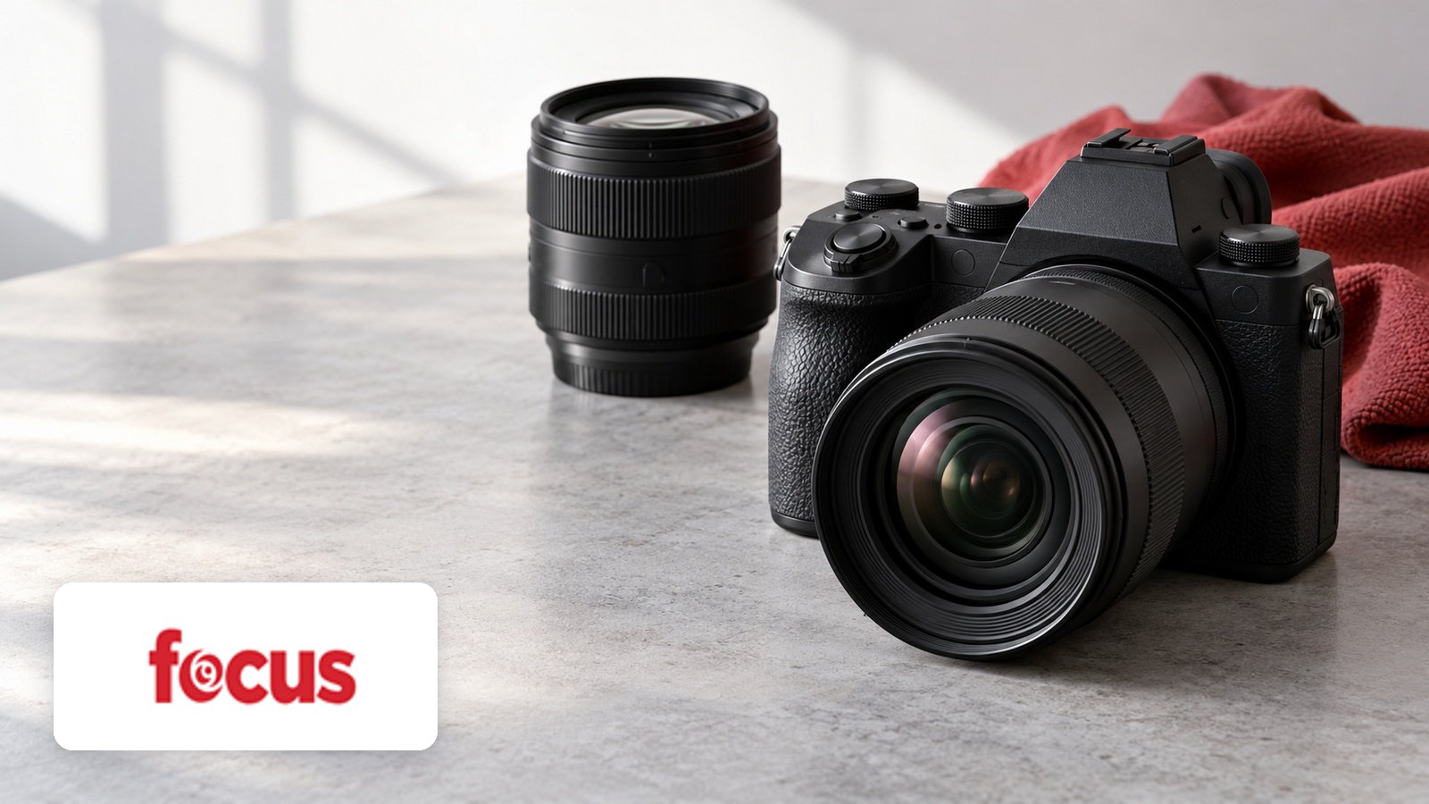 Focus Camera logo with Unbranded black mirrorless camera with zoom lens, spare lens, grey stone table, red cloth